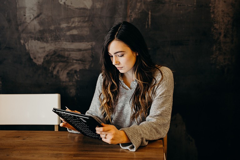 Young woman with long, dark hair, using a stylus on her laptop tablet.