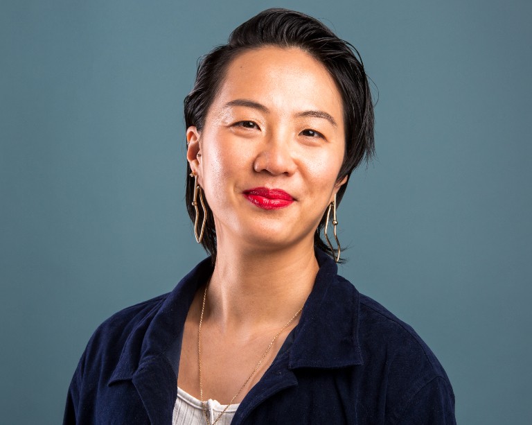 Smiling woman wearing navy collared shirt with gold earrings and necklace