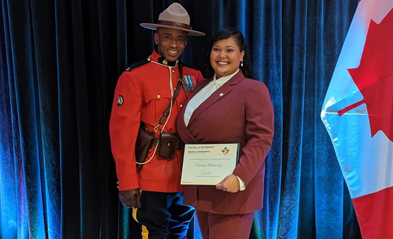 Young smiling woman holding an award certificate and standing with a smiling man wearing the Canadian Royal Mounties uniform.