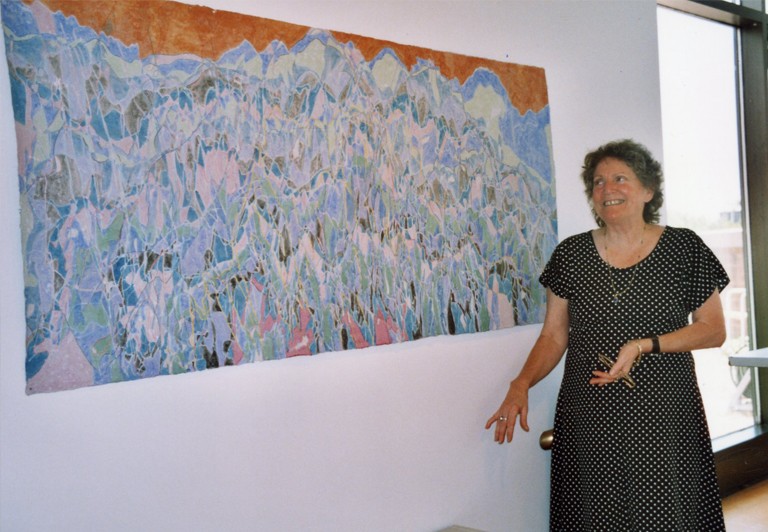 A women in a dotted dress stands next to an abstract art piece that appears to feature mountains.