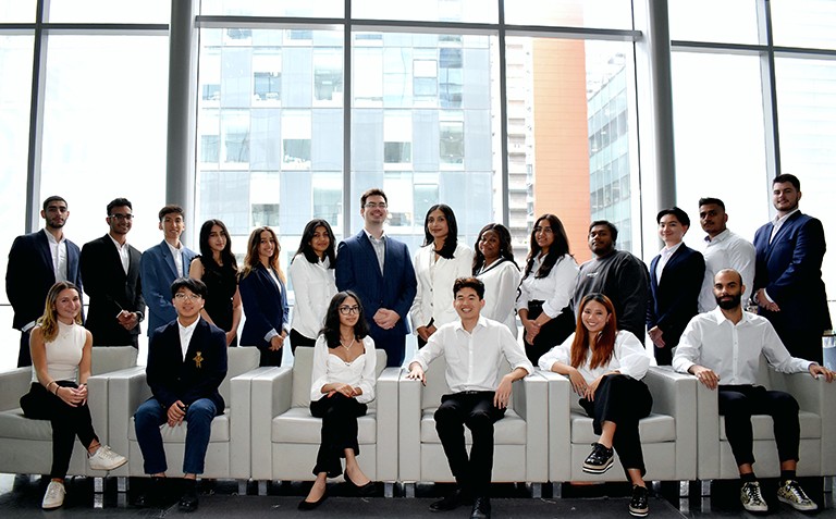 A large group of young men and women posing for the photograph. The first row is seated on white leather armchairs and the back row is standing.