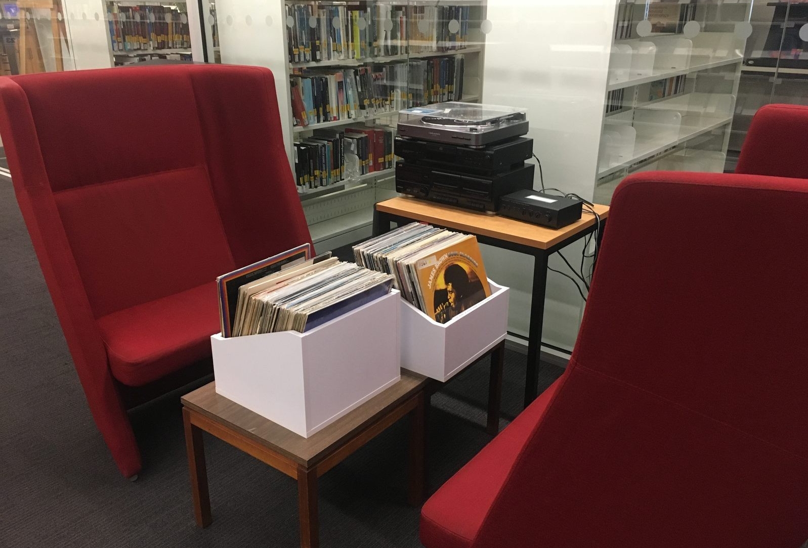 Large red armchairs with a turntable and a box of LPs on a desk, and shelves of books in the background