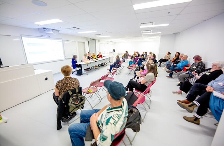 A group of people sitting in a classroom setting and watching a panel presentation.