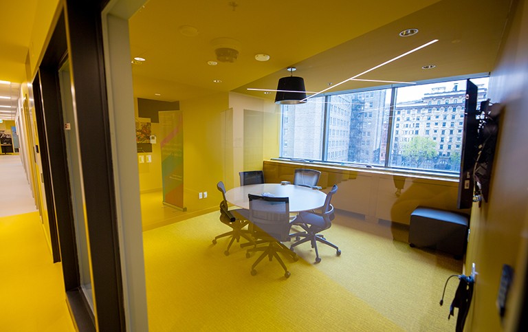 Interior of a building looking into a meeting room space through yellow panes of glass.
