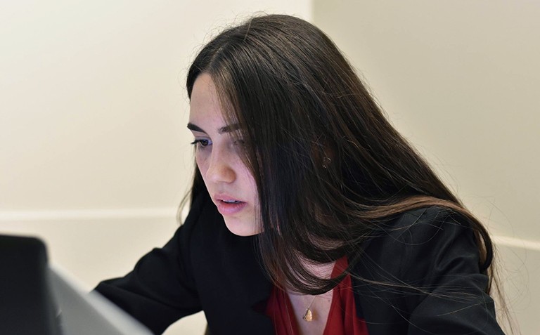A young woman with long, dark hair looking intently into the screen of a laptop