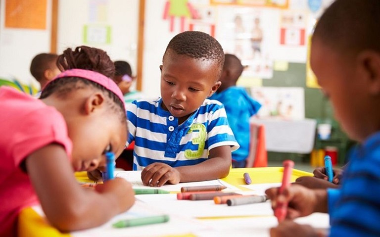 Young children sitting around a table and drawing with crayons.