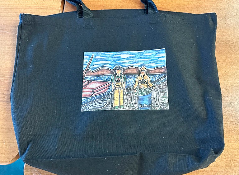 A black tote bag with a graphic image sewn on the front.