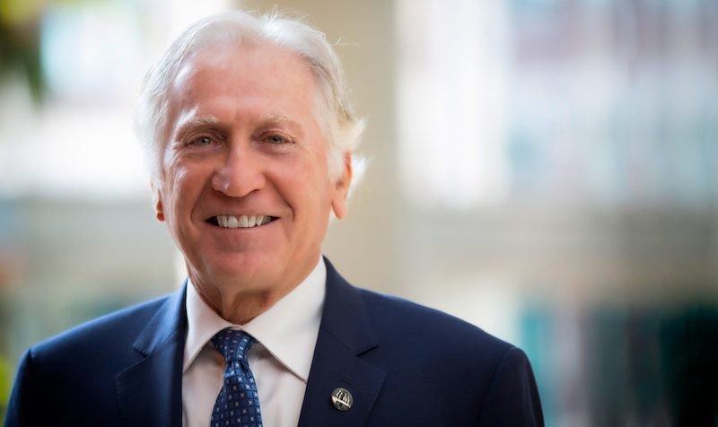 Smiling man with short, greying hair, wearing a suit and tie.