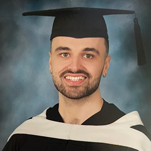 Young smiling man with a beard and wearing a graduation gown and cap