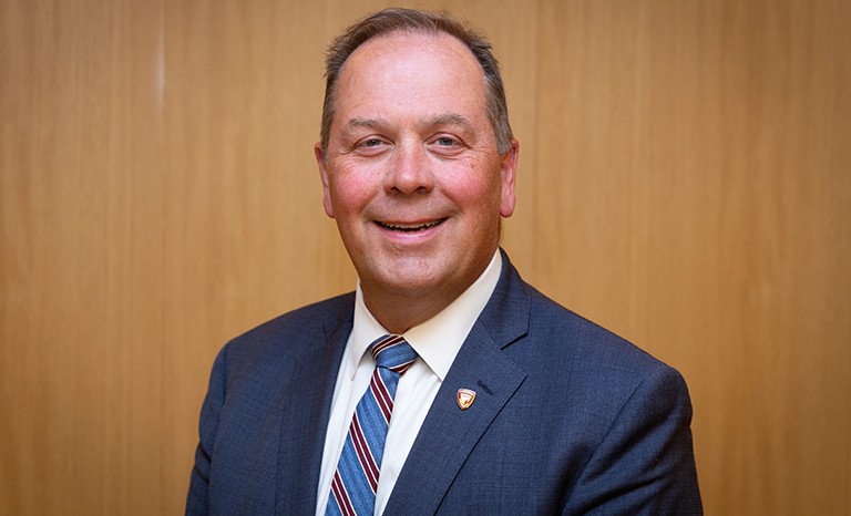 Smiling man with short, greying hair, wearing a suit and tie.