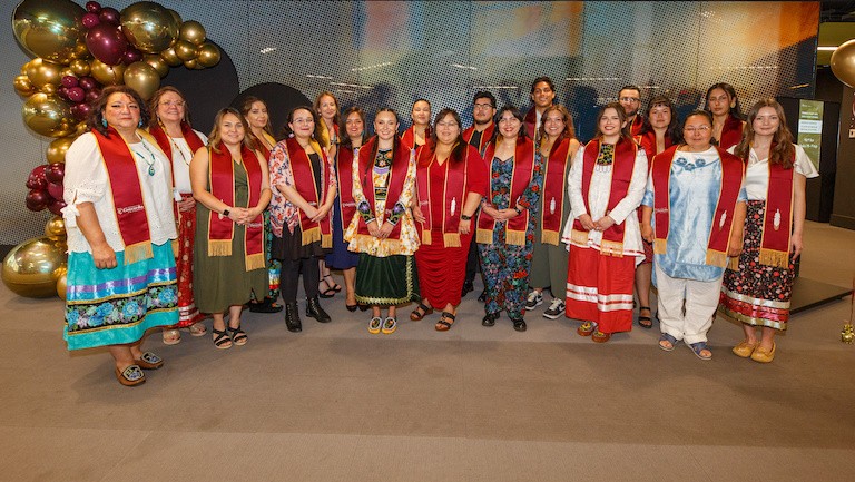 A group of indigenous graduates pose for a photo wearing the related regalia 