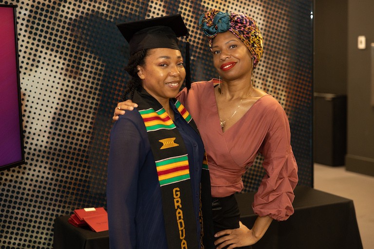 Two black women, arm in arm, smile for the camera