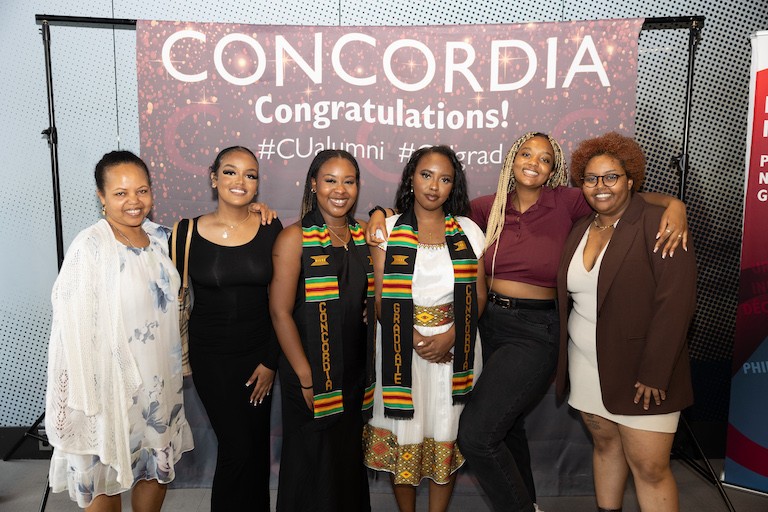 A group of six young black women, smiling in front of a Concordia backdrop