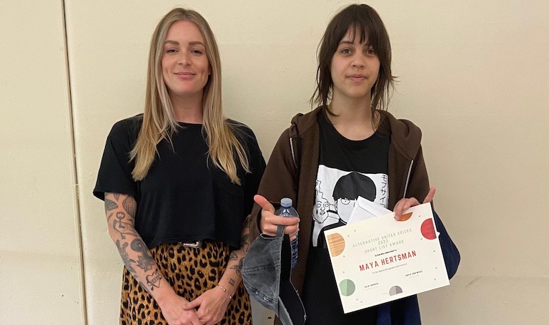 Heather Hardie with her student, Maya Hertsman, who created the cover art for <i>Voices</i>. Two young women smiling at the camera, one holding an award certificate