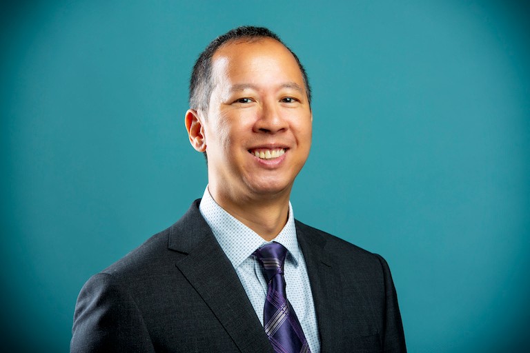 A portrait of a smiling man wearing a suit, with a turquoise background