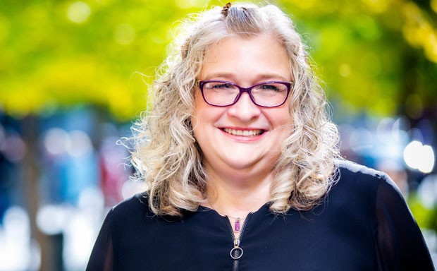 Smiling woman with long, blonde, curly hair, wearing red-rimmed glasses and a black top