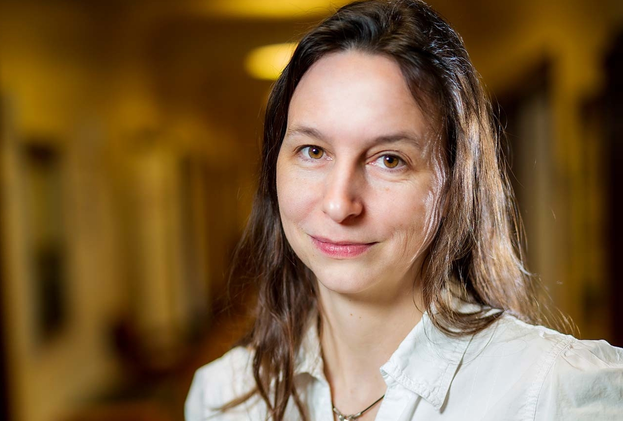 Rebecca Tittler: “Knowledge of the non-human living world provides well-being, a feeling of being grounded and rooted, if you will. This is something we all need.” Smiling woman with long dark hair, wearing a red top.