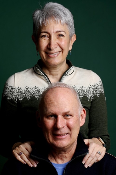 Woman with short, grey hair standing behind a man with her hands on his shoulders.