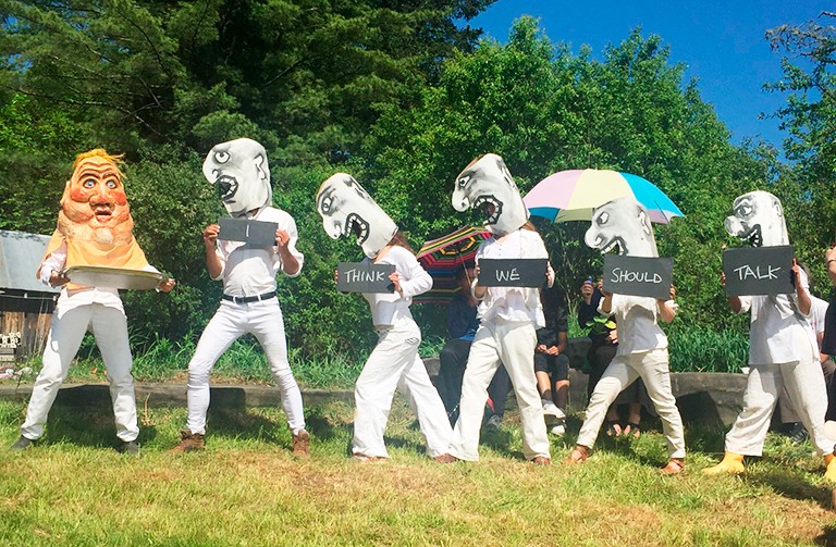 A group of people with large puppet heads each holding a sign that makes the sentence, "I think we should talk."