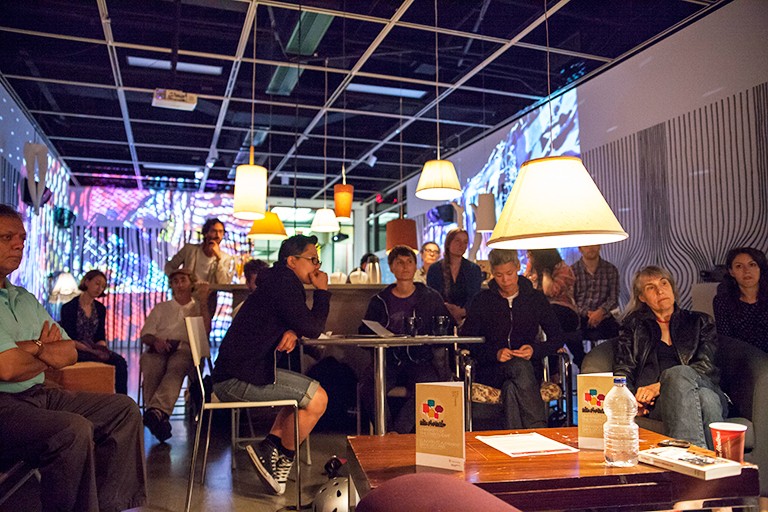 A diverse group of people sitting in a cafe setting at night and having a discussion together.