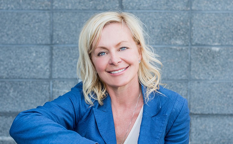 A smiling woman with long blonde hair, blue eyes and wearing a white top and blue blazer