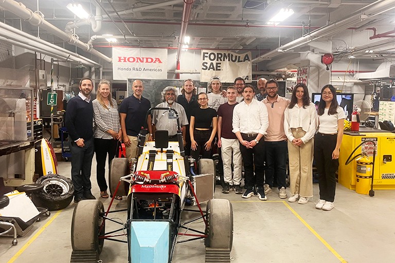 A group of men and women standing in an interior garage space and smiling for the camera.