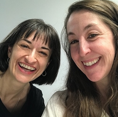 Two women, one with shoulder-length dark hair, one with long, dark blonde hair, smiling for the camera.