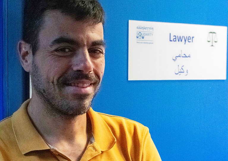 Apostolos Veizis, executive director of INTERSOS Hellas: "We get stories of people that have been looking for months to find a shelter. " / Photo by Lucas Marsh A man stands in a blue doorway, smiling at the camera