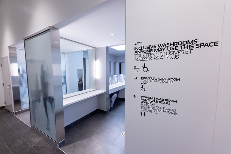 A bathroom space with a sign that says, "Inclusive washrooms, anyone may use this space. Toilettes inclusives et accessibles a tous."