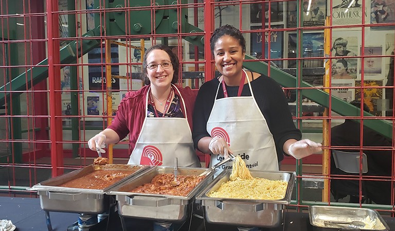 Two women posing for a photo while serving pasta