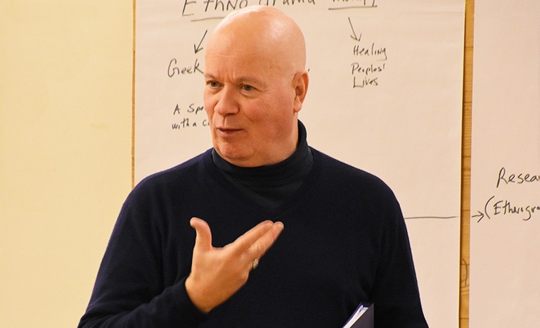 A man with a black turtle neck teaching to a class.