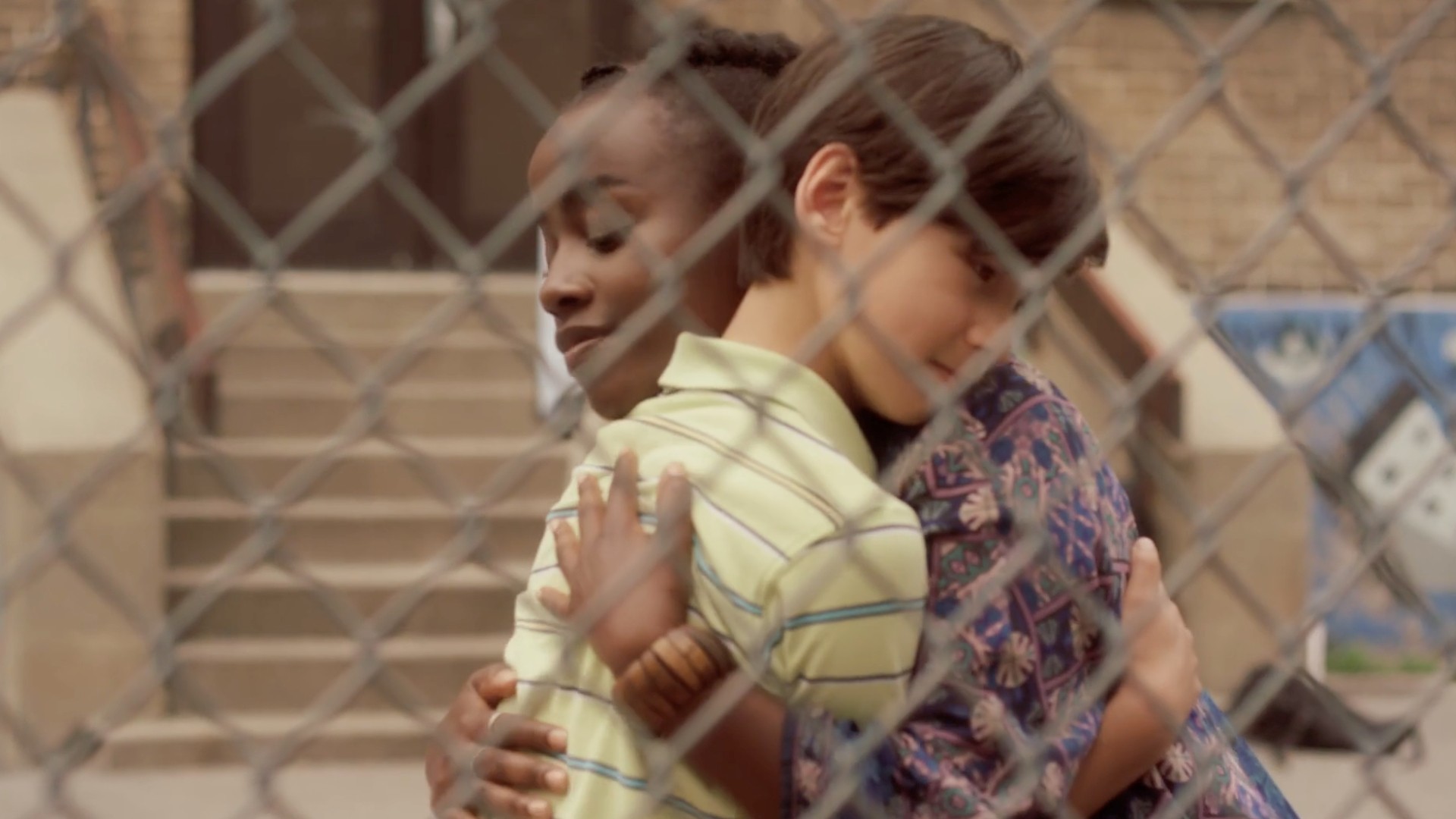 A young woman and a boy of around 12 years of age share a hug, as seen through a chainlink fence.