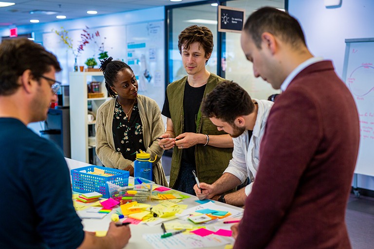 Group of standing adults circled around a table with colourful Post-It notes and permanent markers