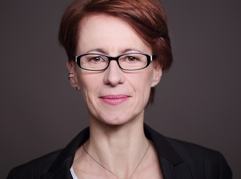 Smiling woman with short red hair and glasses, a white top, a black blazer and a silver necklace
