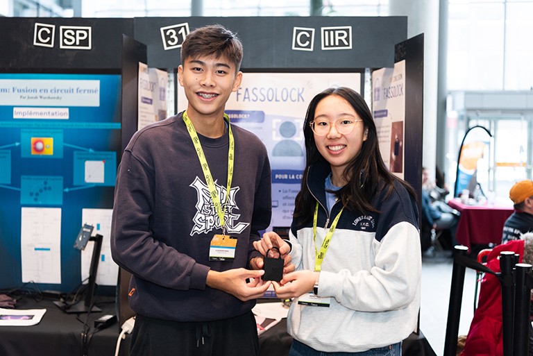 A young man and woman standing in front of a science project and holding a large black lock