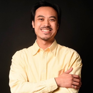 Smiling man with short, dark hair, a beard, and wearing a yellow button-down shirt.