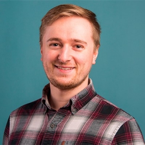 Smiling young man with short, blond hair and a beard, wearing a checkered shirt