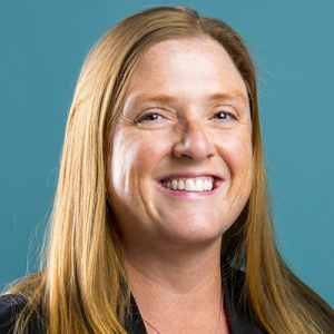Smiling woman with long strawberry blonde hair, wearing a dark blazer.