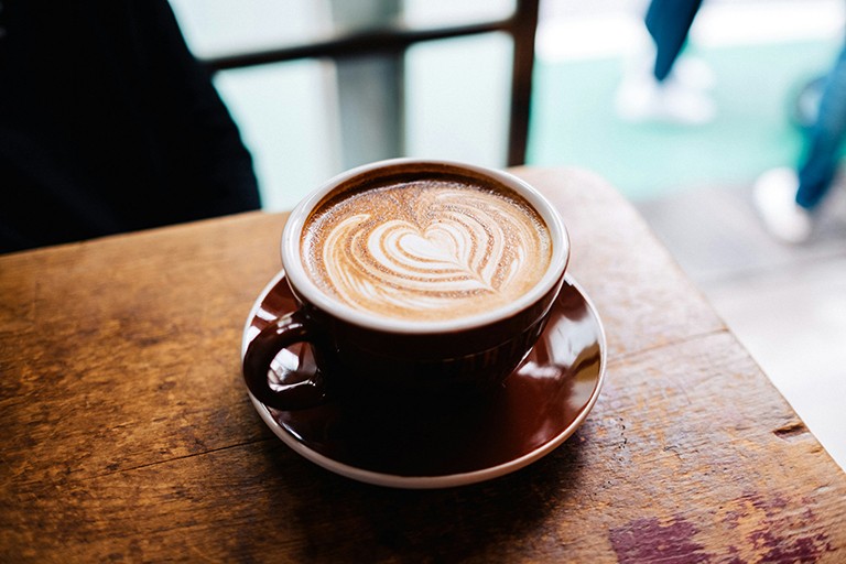 A latte coffee in a porcelain cup on a table, with the milk froth shaped like a heart.