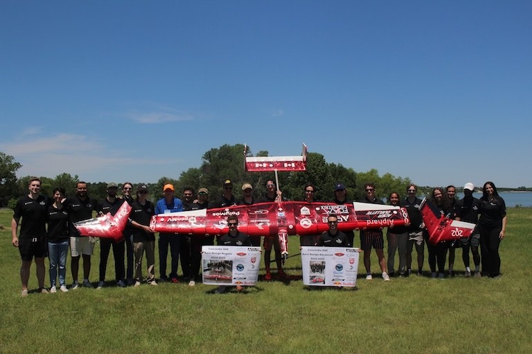 A group of students holding up a small red airplane.