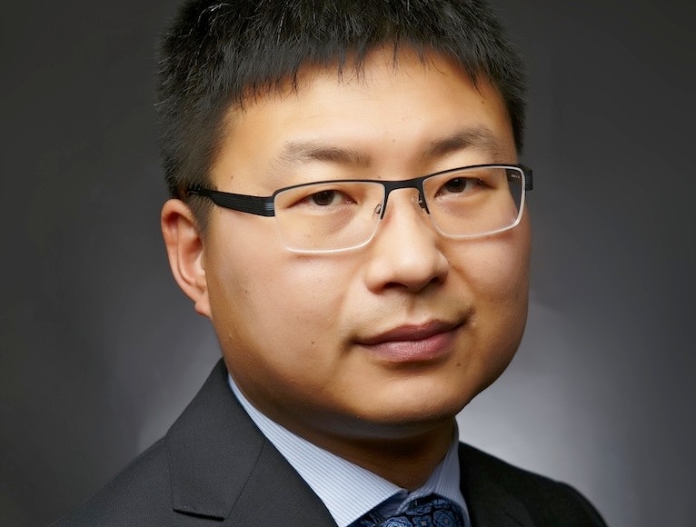 Chunjiang An: “A major part of our research is listening to the communities and understanding their priorities.” Smiling Asian man with short dark hair, wearing a grey suit and blue tie