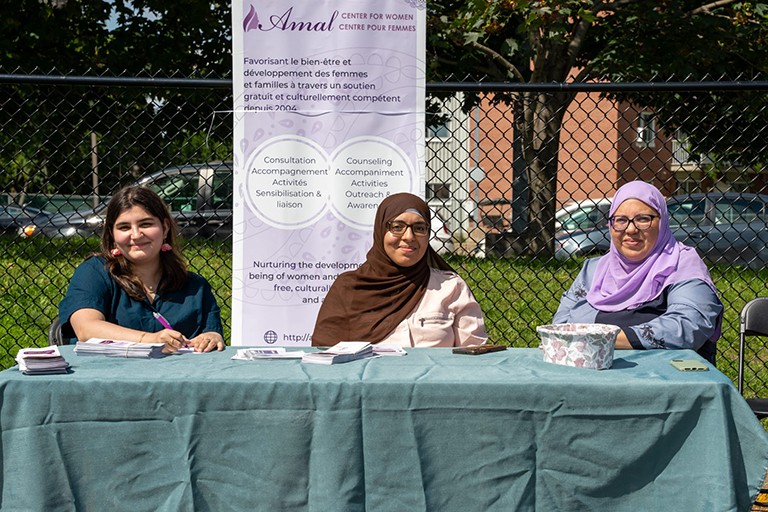 Three women sitting at an information table in the outdoors.