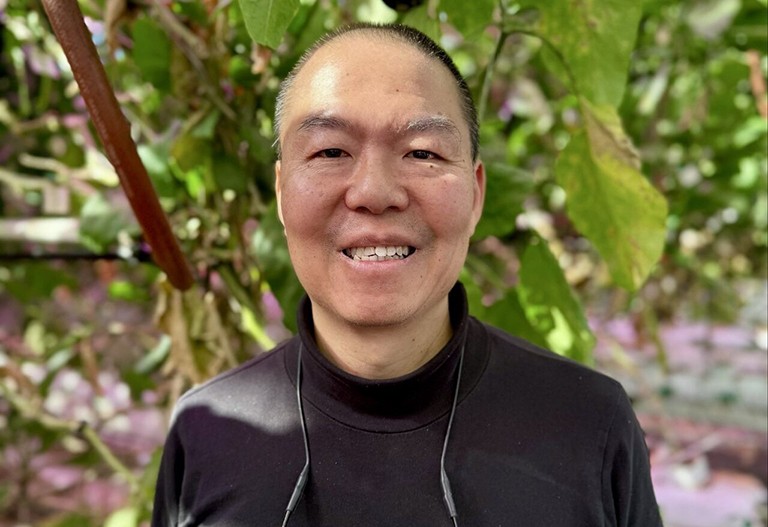 Smiling man in a black top with green vegetation behind him