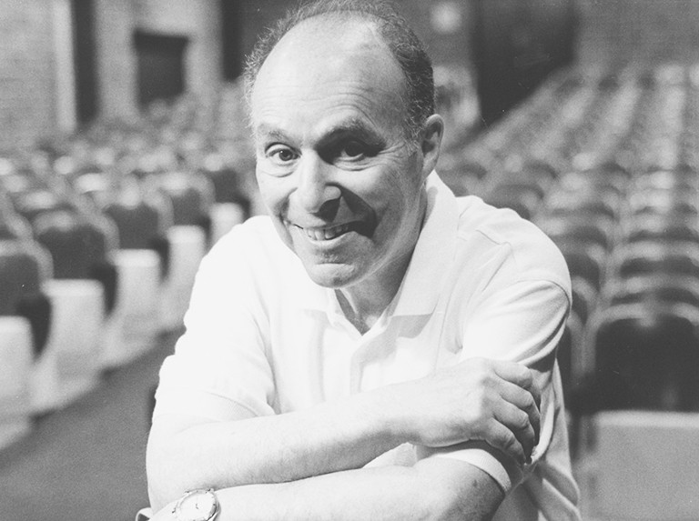 A black and white archival photo of a smiling man with thinning hair and wearing a white polo shirt.