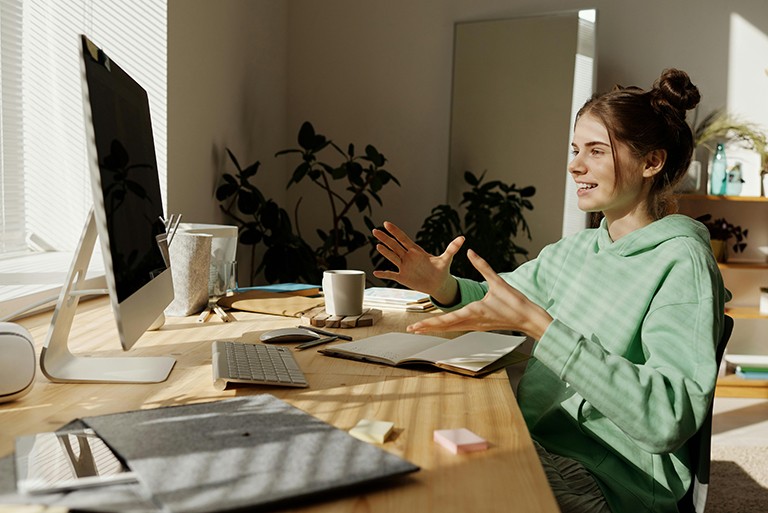A young woman sitting at a desk and talking to her computer screen