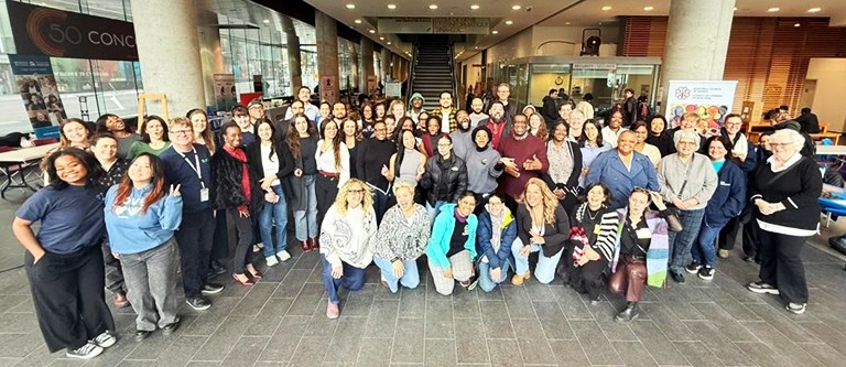 A large group of people standing together in an indoor atrium and smiling for the camera