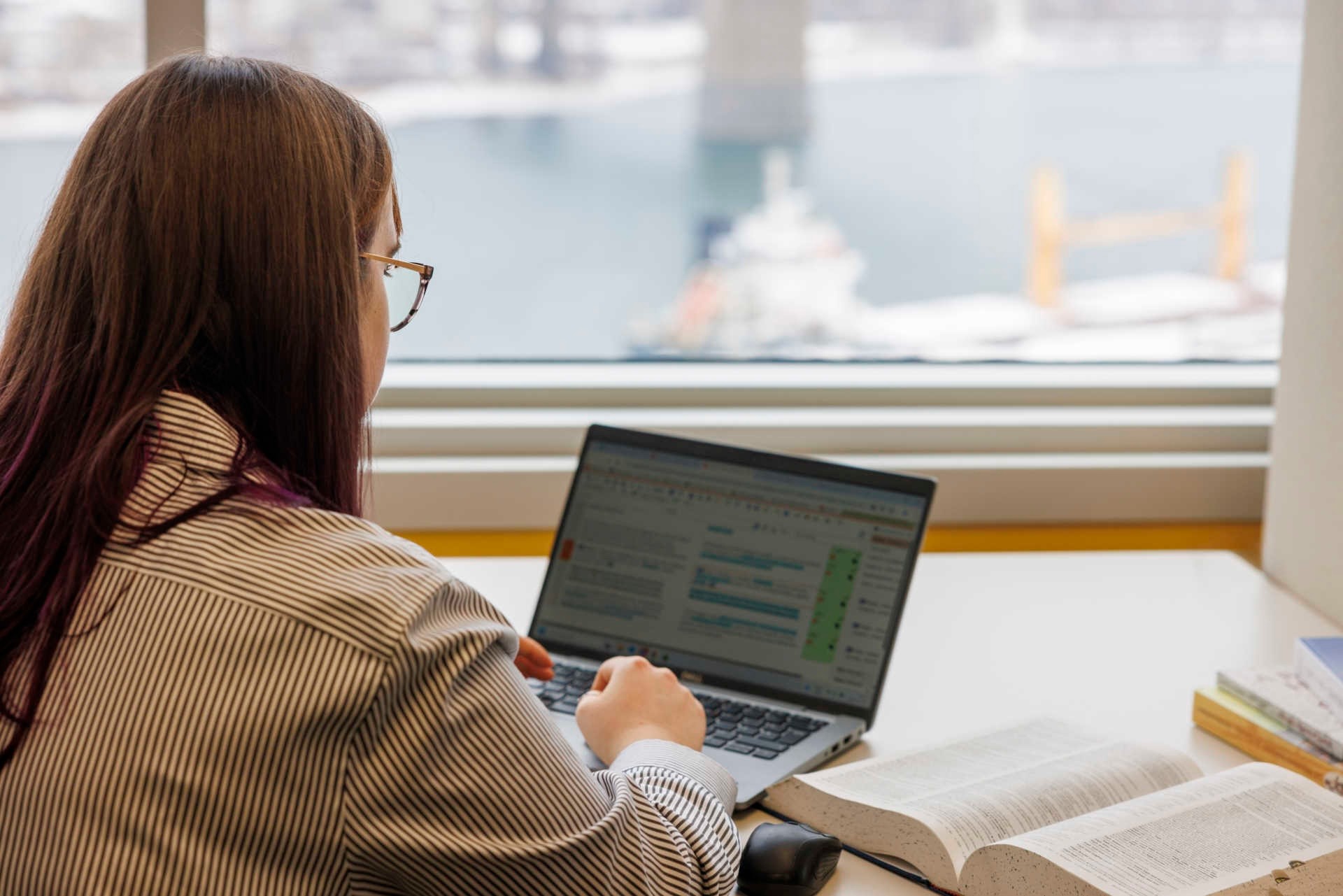 A young woman sitting in front of a window at a laptop computer