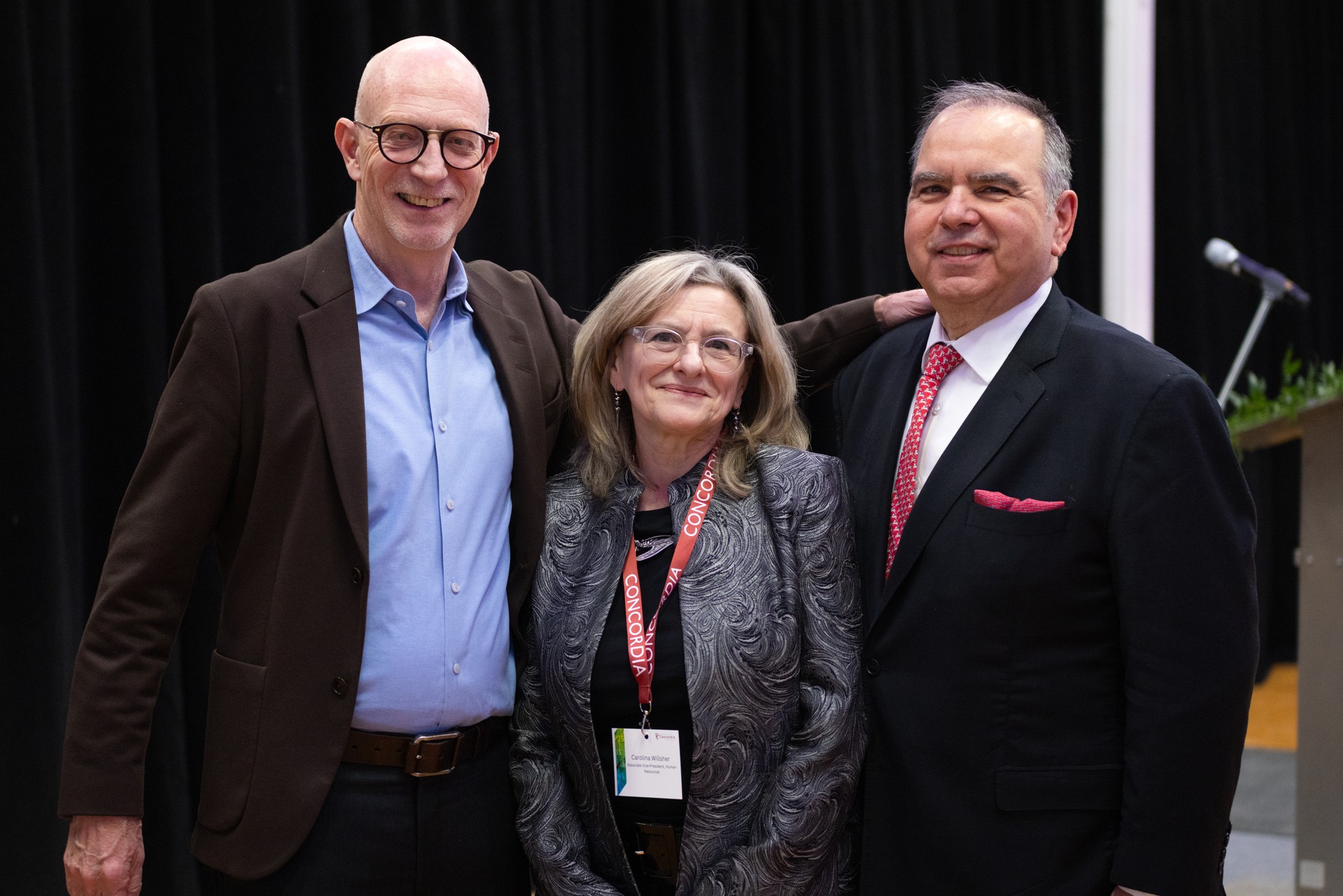 Three people standing together and smiling at an event.