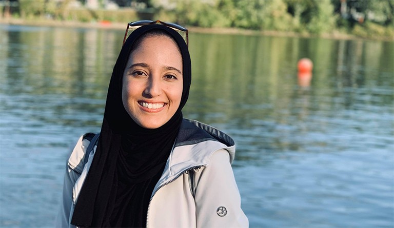 Young, smiling woman in a headscarf, with a lake in the background.