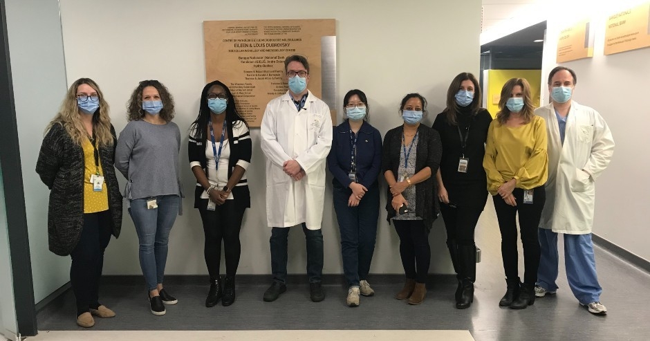 Nine healthcare workers wearing blue masks face the camera in the OPTILAB.
